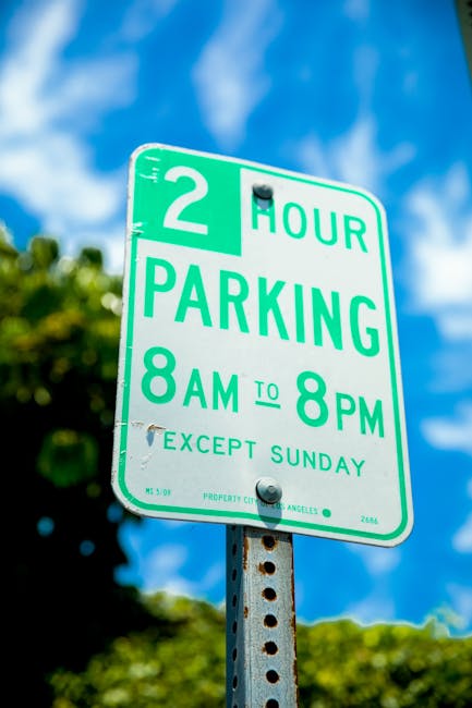 Four blue parking signs with white lettering and symbols are mounted on black metal poles against a vertically ridged, metallic grey building wall. The signs display a large 'P' and include additional
